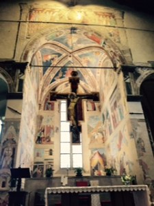 Basilica de San Francesco in Arezzo with a suspended cross in front of the altar which is surrounded by frescoes painted by Piero della Francesca